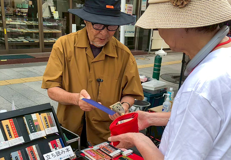路上で対面販売をする作家と赤い財布を手に取る来場者