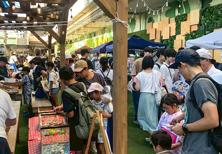 緑豊かな屋外会場で多くの来場者が買い物を楽しむ賑わいの様子